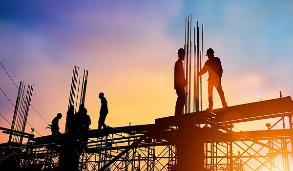 Construction workers on a reinforced concrete slab with steel reinforcement bars rising against an evening sky