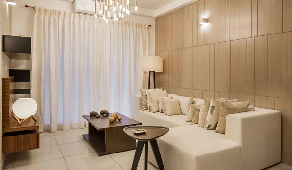 Neutral-toned living room with a sectional sofa, timber-panelled wall, floor lamp and sheer curtains over a full-height window