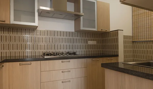 Modular kitchen with light timber cabinets, a dark stone counter, tiled splashback, gas hob and chimney hood